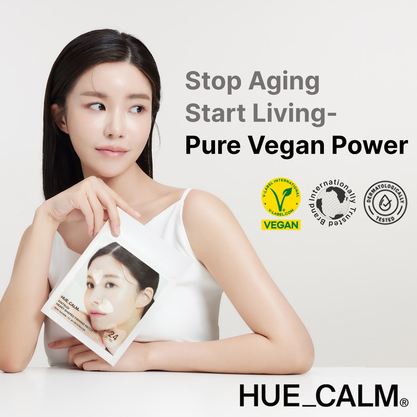 Model holding Hue Calm heart-shaped anti-wrinkle patch pouch with slogan 'Stop Aging, Start Living – Pure Vegan Power' and vegan certification icons