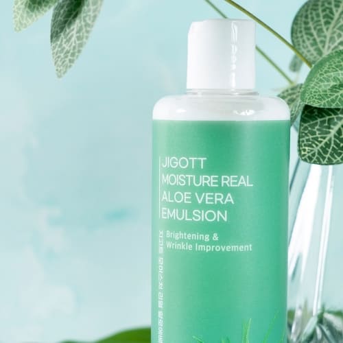 Styled product shot with bottle next to green leaves and glass vase in soft mint backdrop