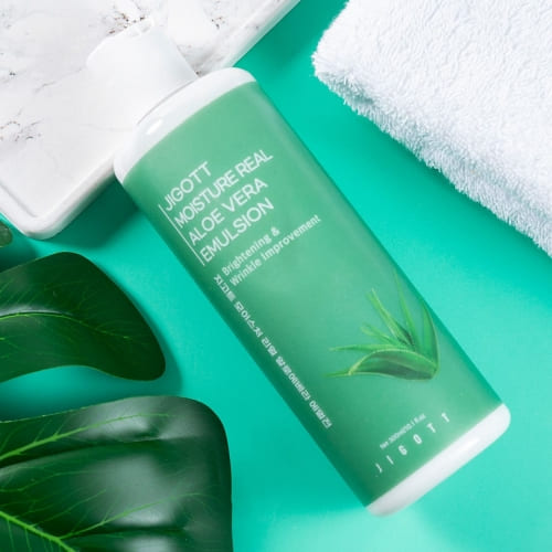 Flatlay of aloe emulsion bottle on green background with marble tray and towel for spa setting