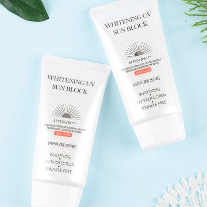 Two Jigott Whitening UV Sunscreen tubes on soft blue flatlay with foliage